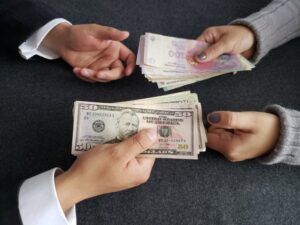 manos entregando billetes argentinos y banco